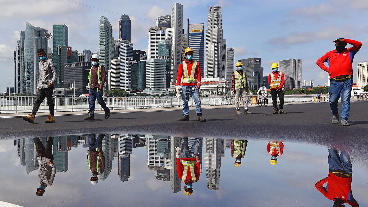 Migrant workers conduct checks on a road surface, with the Singapore city skyline in the background.